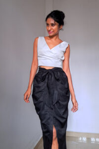 Sia - Pleated Midi Skirt is Black Polyester made with pleats on front and waist band attached sash belt. It has a front slit and zip on the centre back
